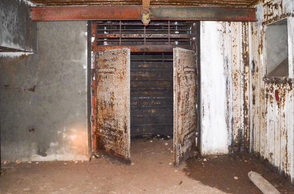 Ligne Maginot - 113 - OLTINGUE - (Casemate d'artillerie) - Chambre de tir coté gauche. Vue donnant sur l'entrée des munitions avec la porte  à 2 battants entrouverte et les rails de protection en place. Cette chambre est plus petite que celle de droite du fait de l'absence de couloir vers l'entrée des hommes qui se fait par la chambre de tir de droite. - D. Froehly